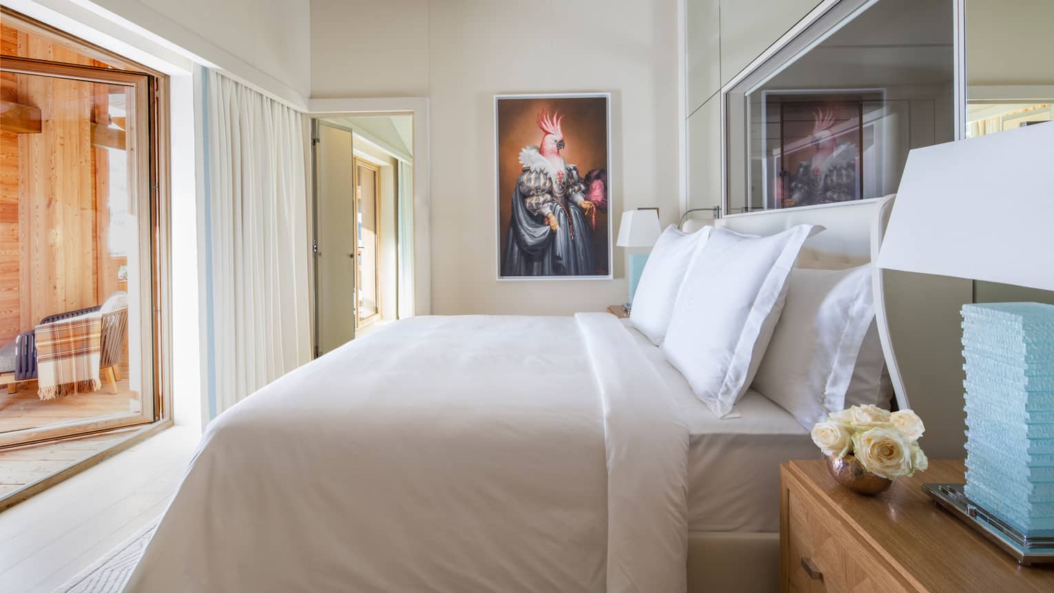 Side view of white-dressed bed, blue lamp beside, portrait on wall at end
