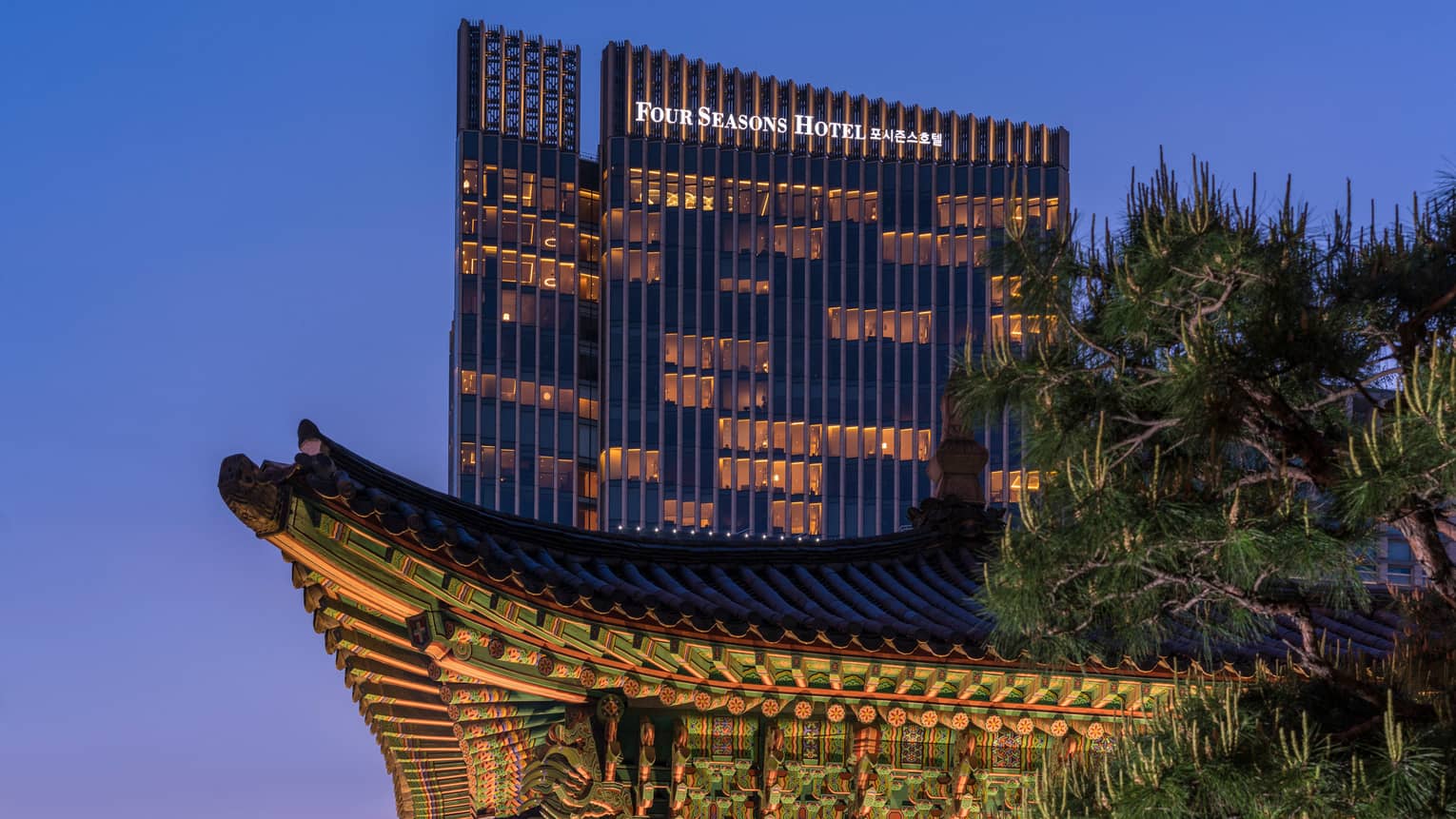 Four Seasons Hotel Seoul modern glass high rise with lights towering over traditional building at night