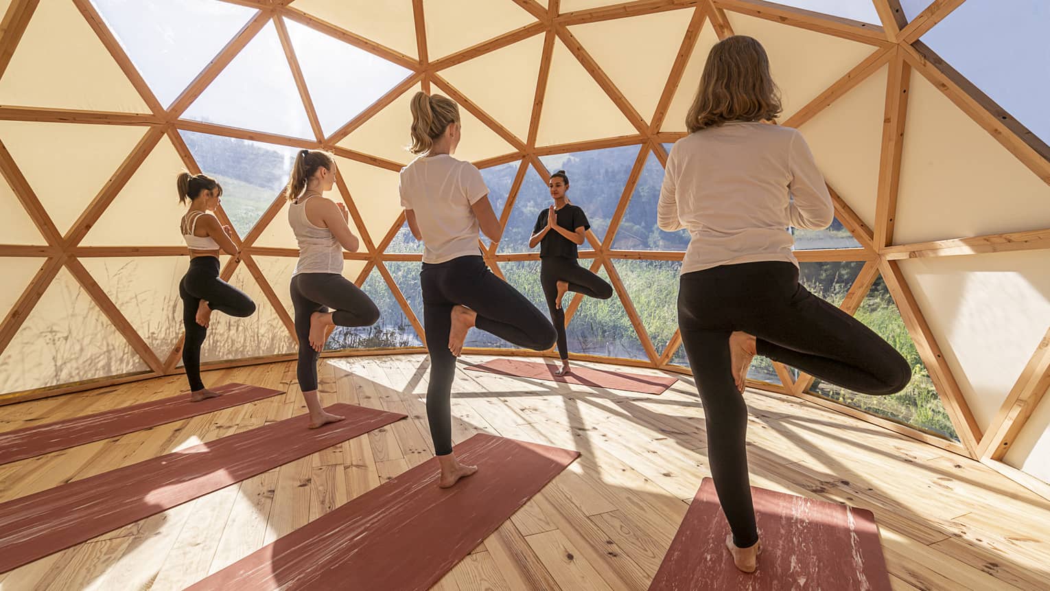 Four women in igloo-like space in standing yoga pose facing instructor