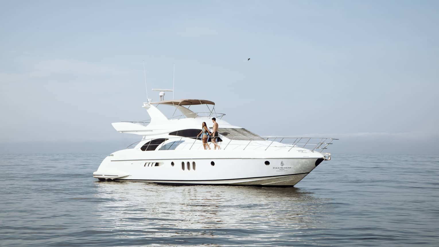 A man and woman standing on the deck of a yacht out on the ocean.