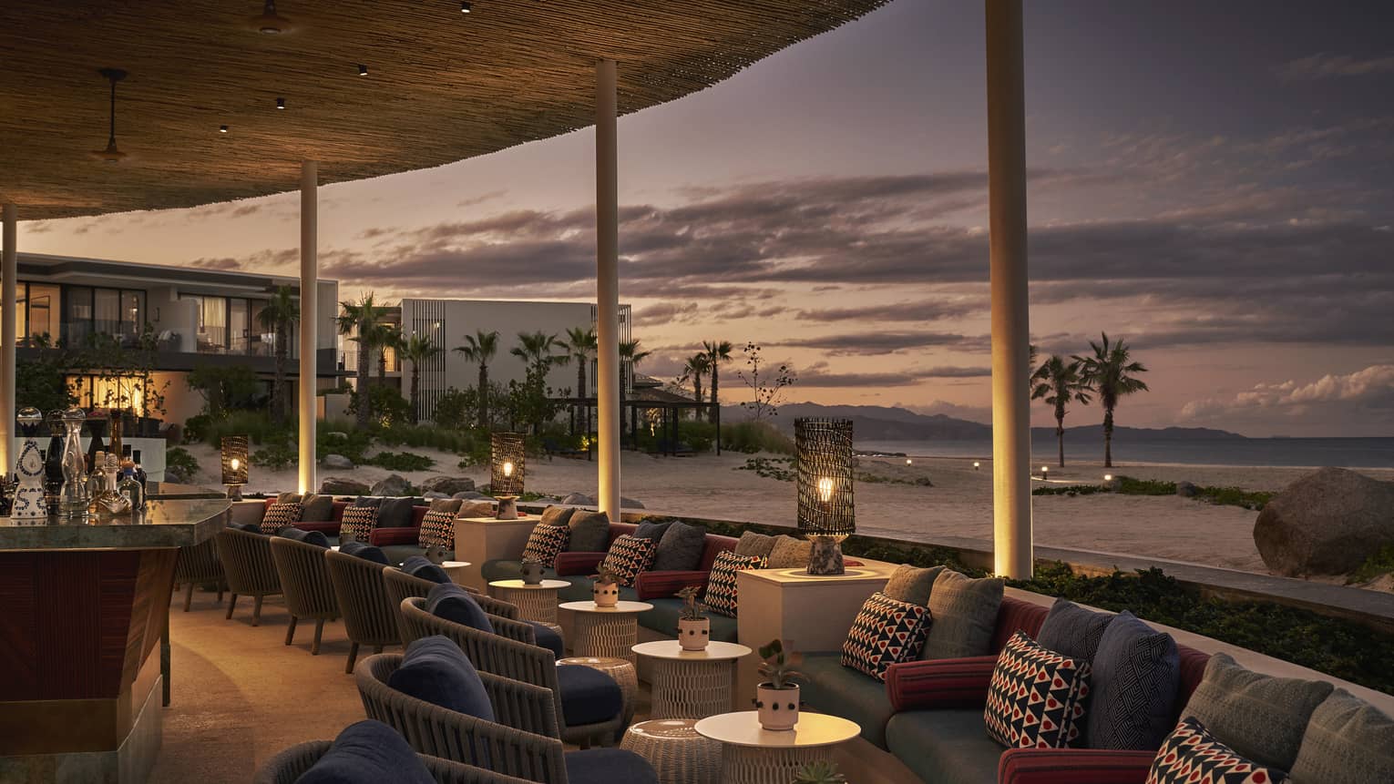 Dimly lit Casa de Brasa lounge area overlooking beach with palm trees at dusk