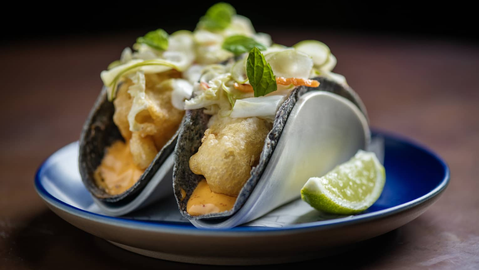 Two crispy fish tacos with aioli and cabbage-chili pickle served on a small blue plate