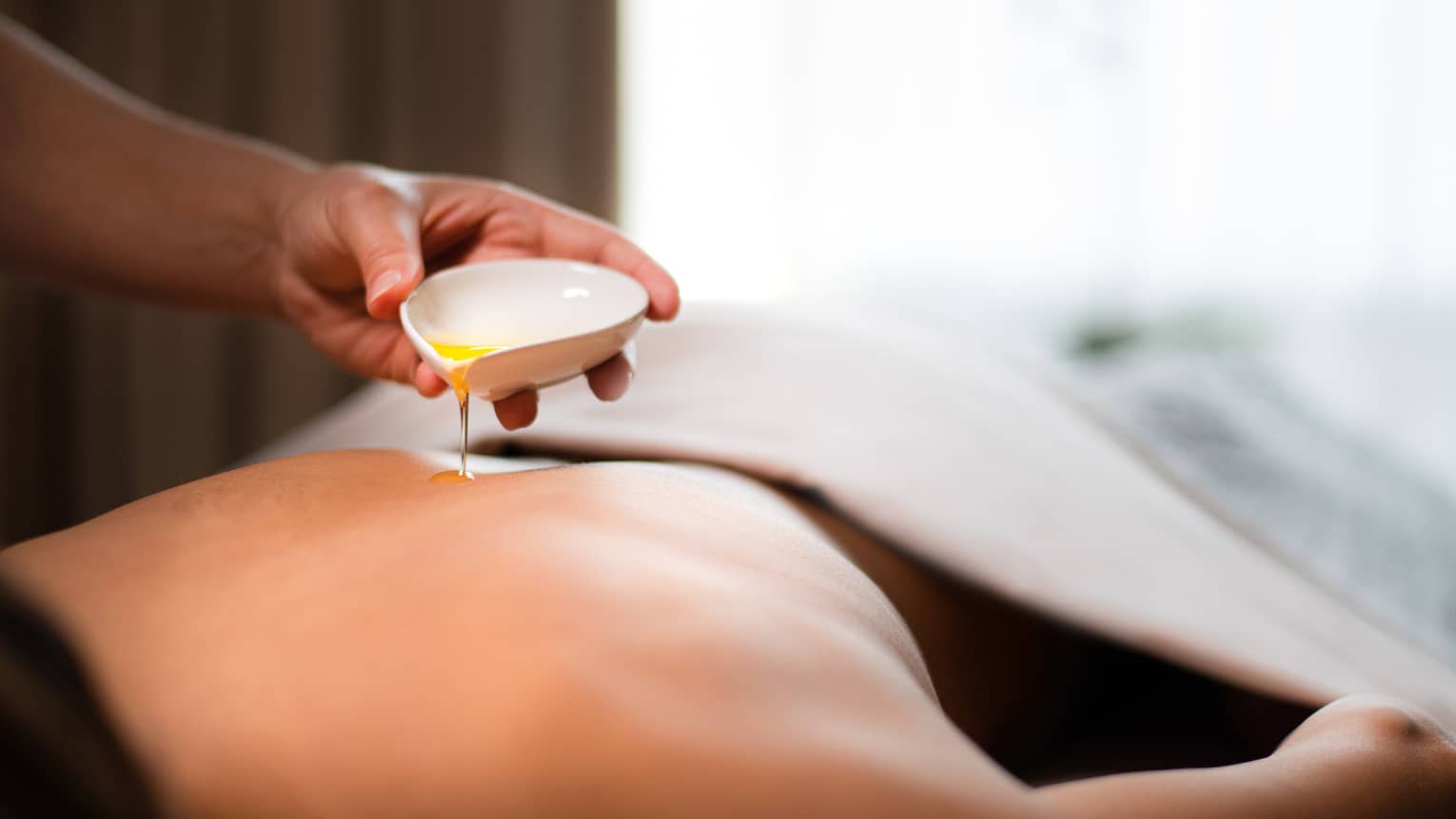 A spa staff member pouring liquid onto a woman?s back.