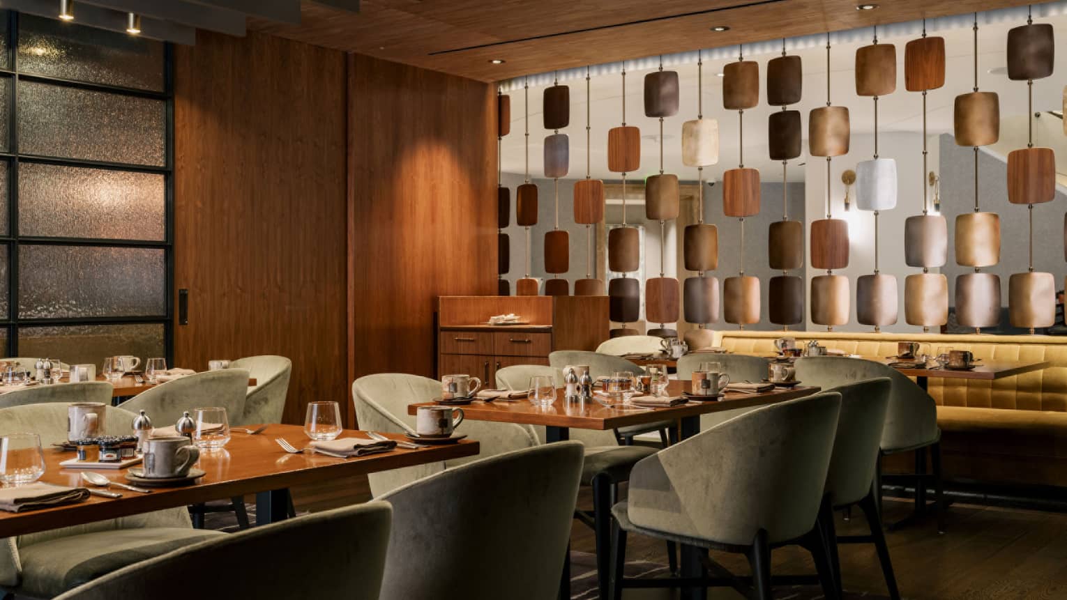Interior of restaurant with sage green chairs, wooden tables, and brass semi-private wall