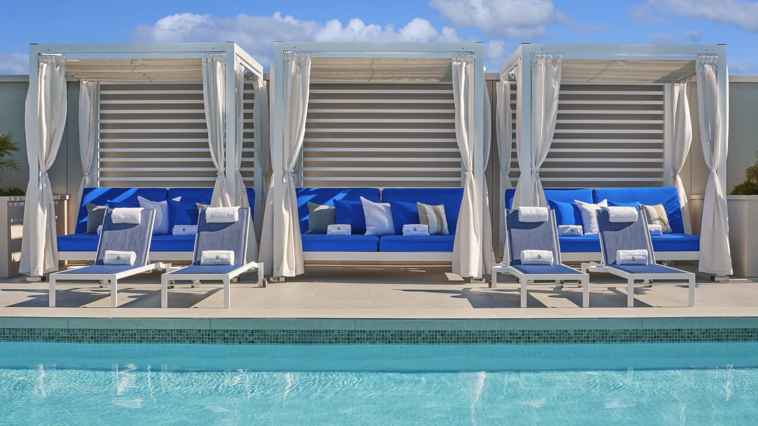 Three blue couches in cabanas by the pool.