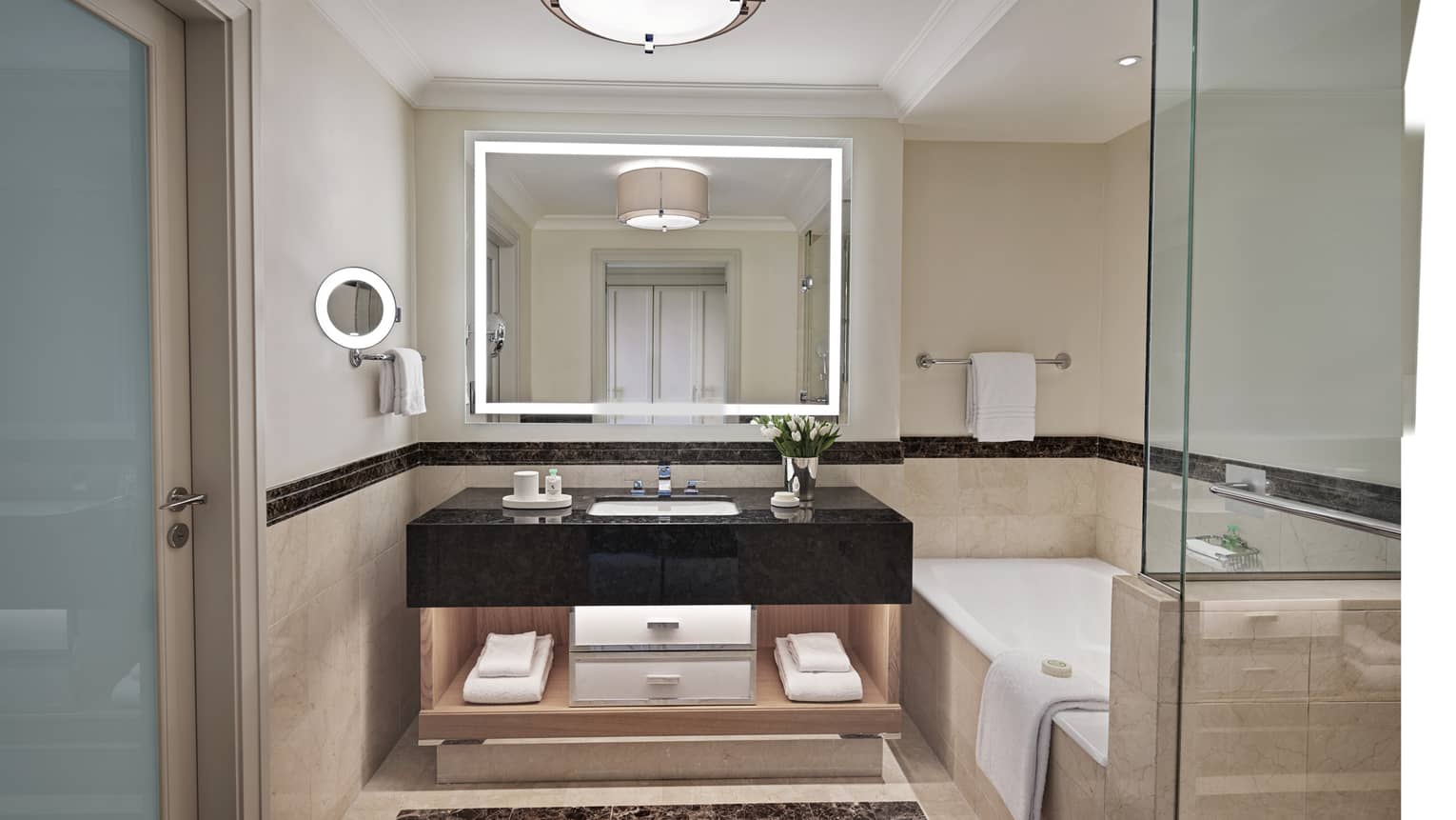 Bathroom with lighted mirror, black marble vanity, tub and separate glass shower