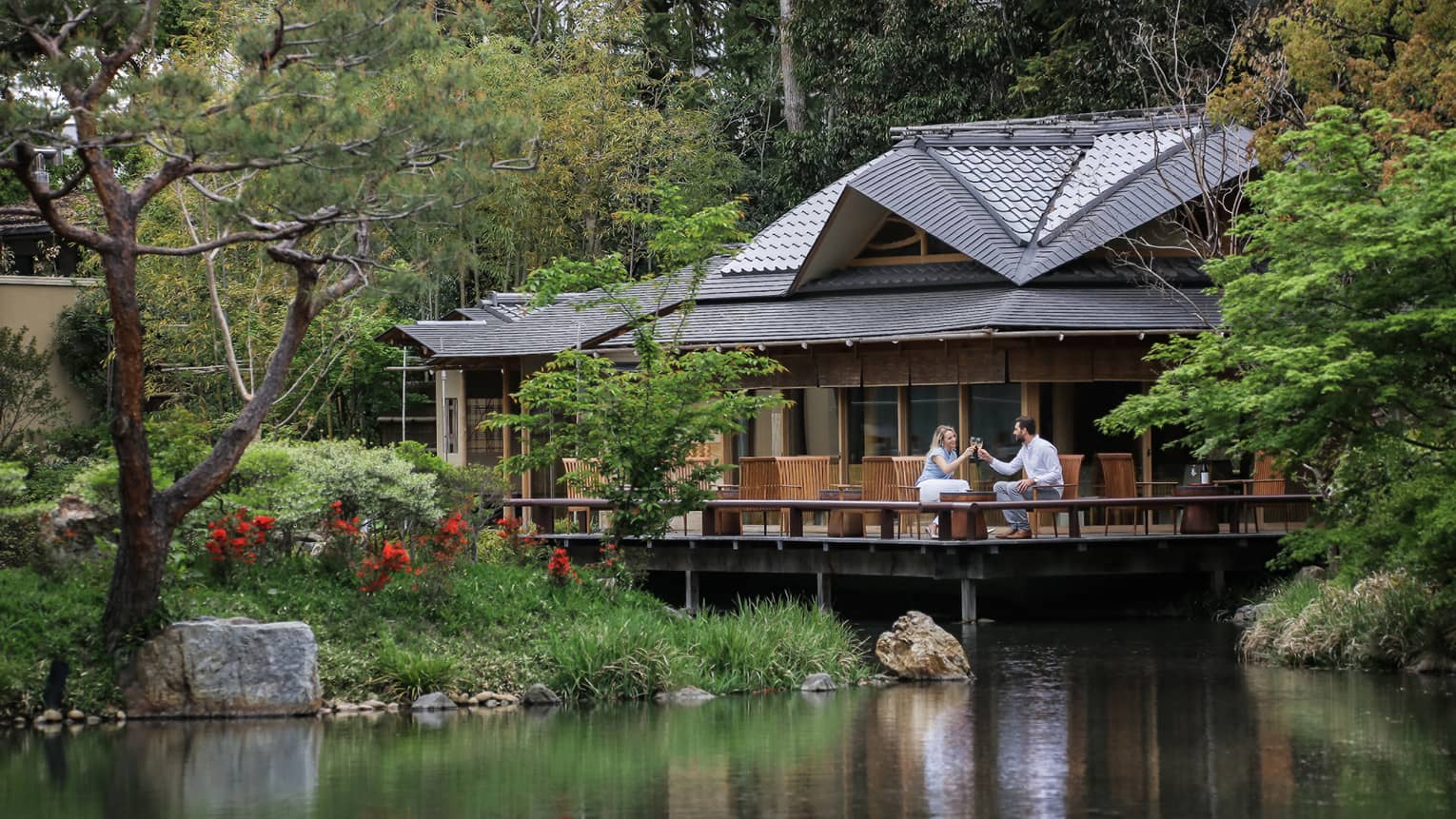 View across pond to restaurant patio where couple toasts with wine glasses