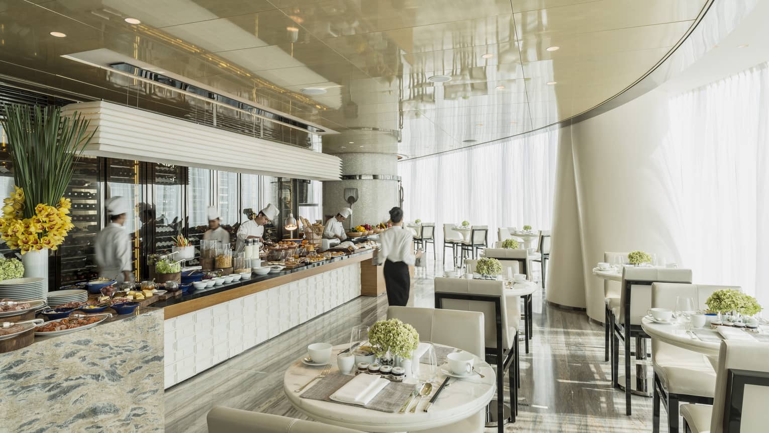 Restaurant dining room with an open live-action kitchen, white walls and chairs, natural light