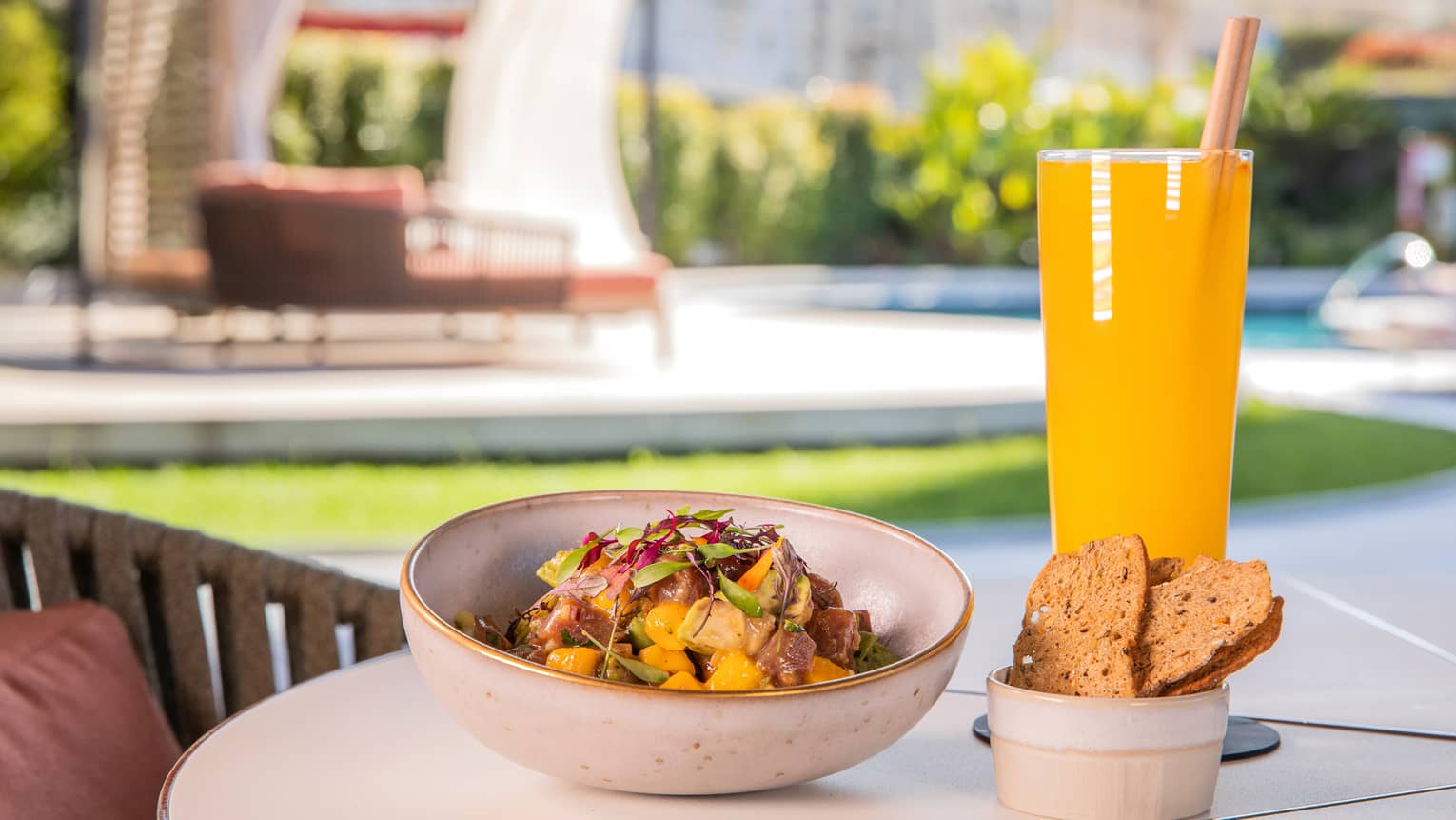 Poolside table set with bowl of tuna ceviche with side of crackers and tall yellow cocktail