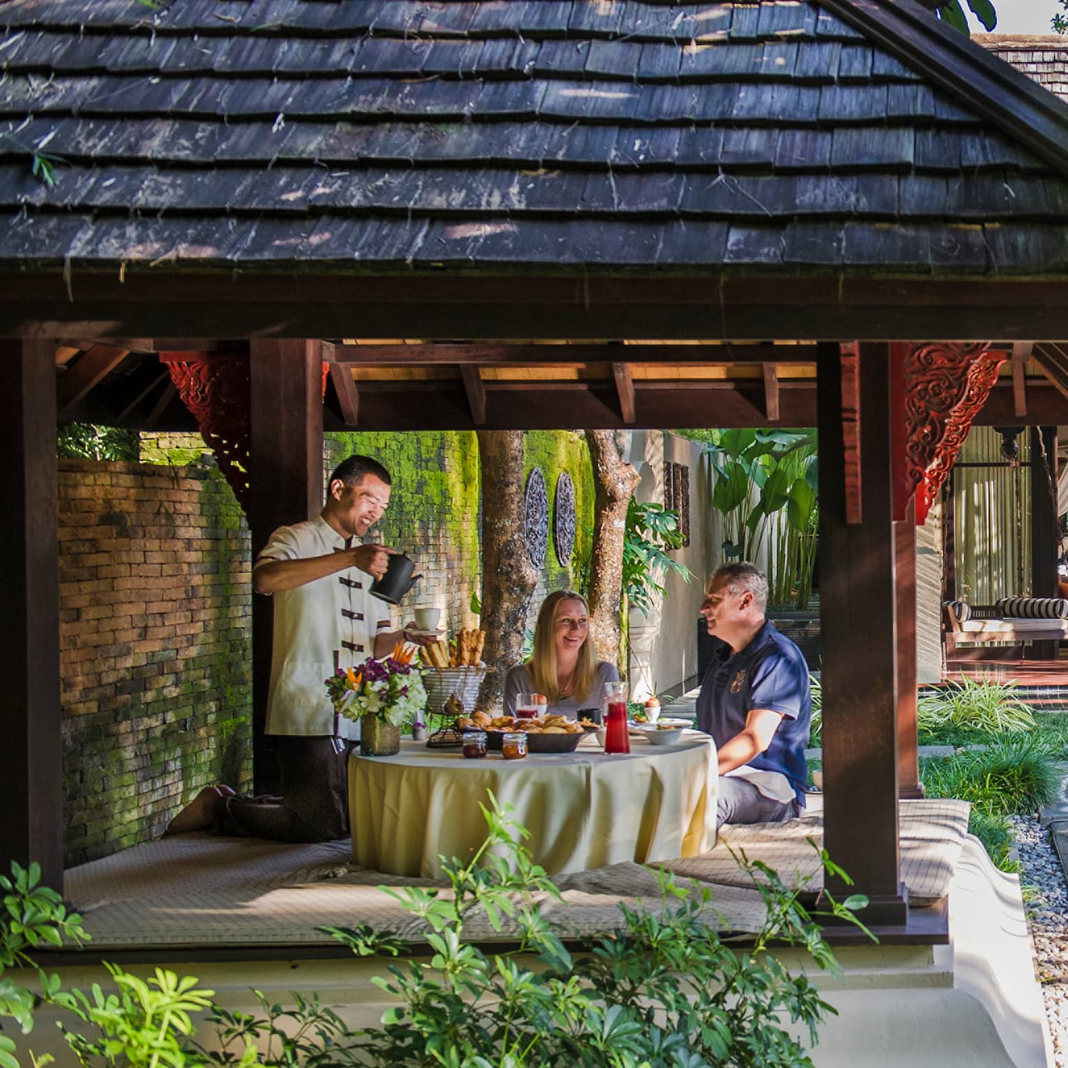 Hotel staff serve couple under dining gazebo by pond