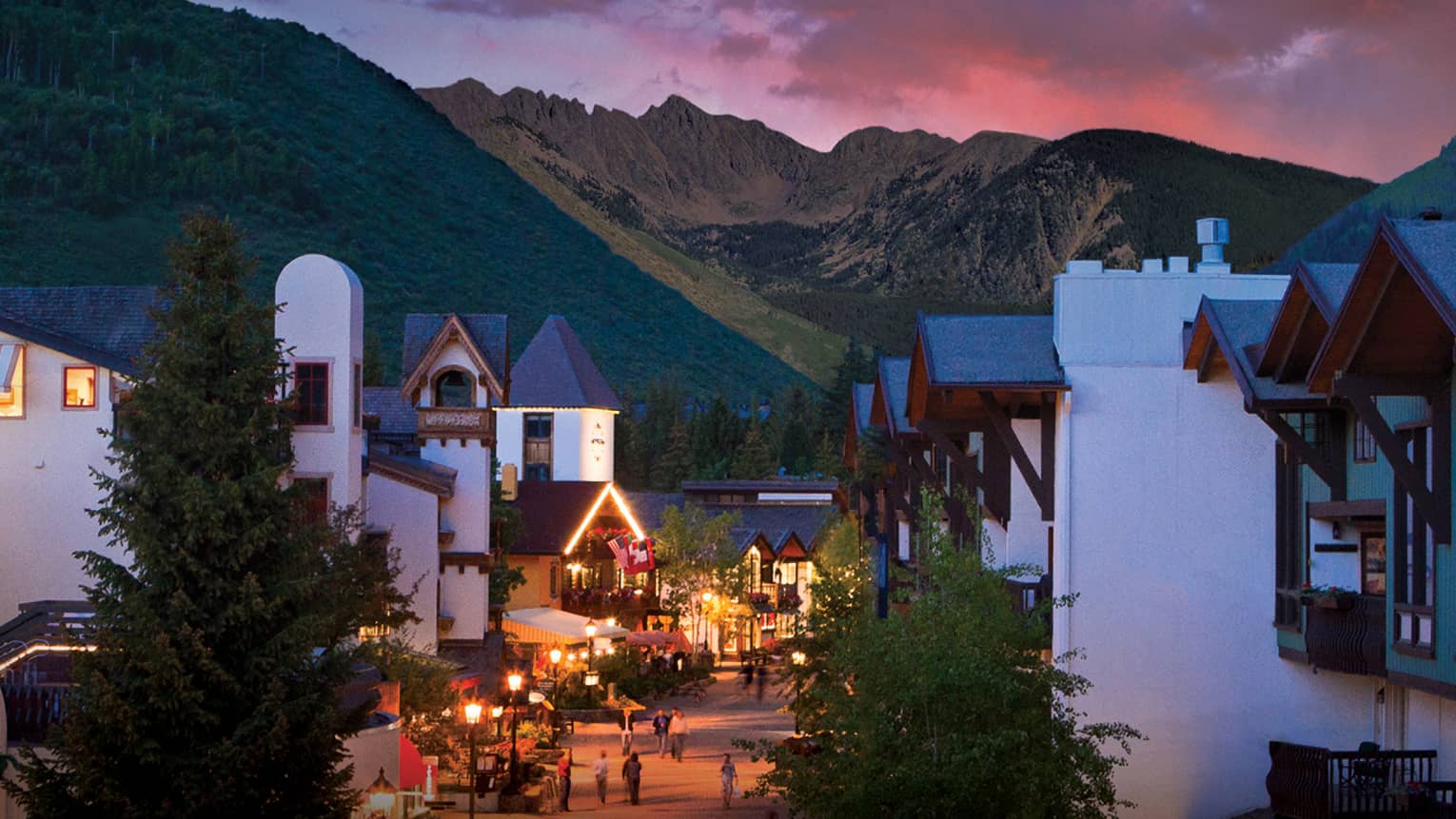A sunset over a small village like city center with white buildings and mountains in the distance.