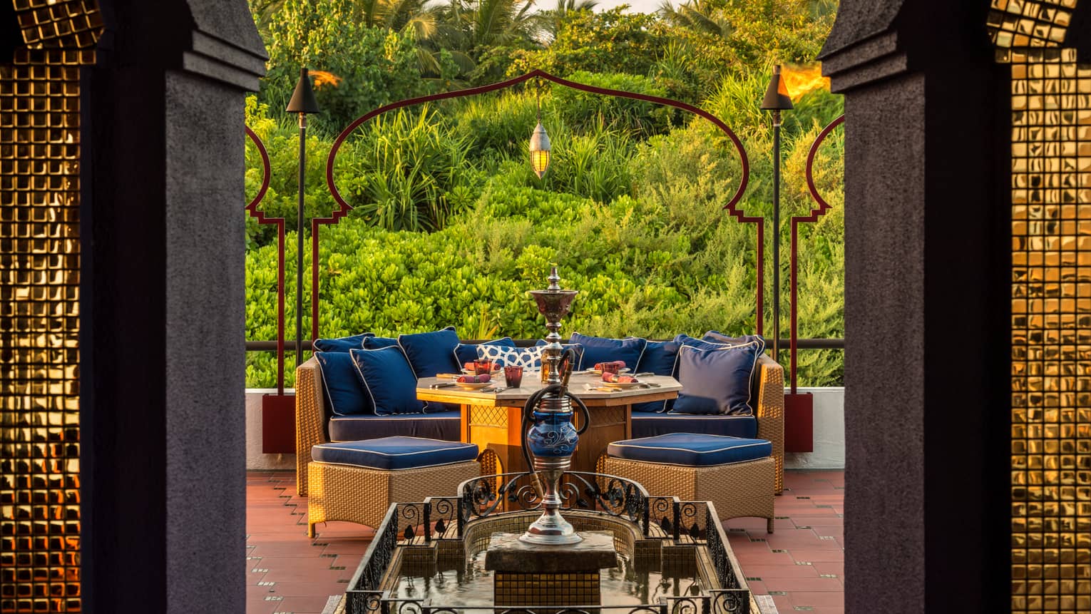 Shisha pipe on platform in front of plush blue patio sofa, dining table, tropical gardens