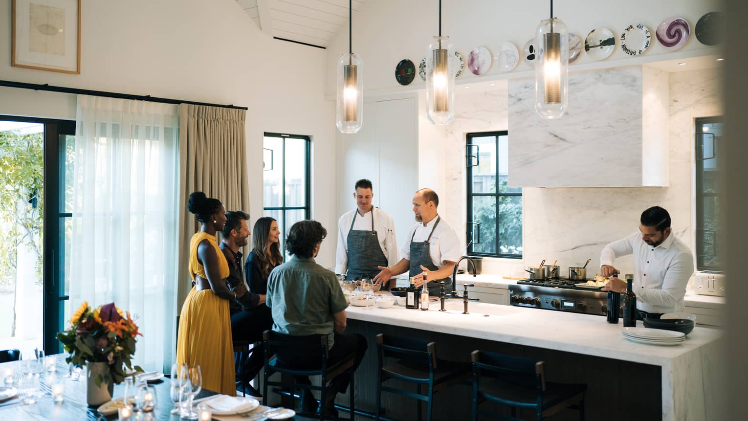 People gathered around the kitchen island where chefs are preparing a meal