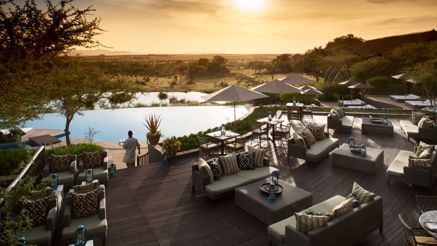 Server carries tray through Terrace Bar outdoor patio by lounge chairs, swimming pool at sunset