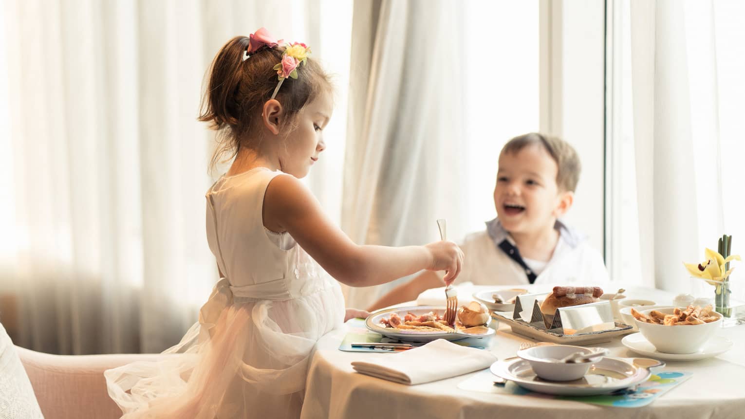 Smartly dressed young boy and girl enjoy sweet treats at a table 