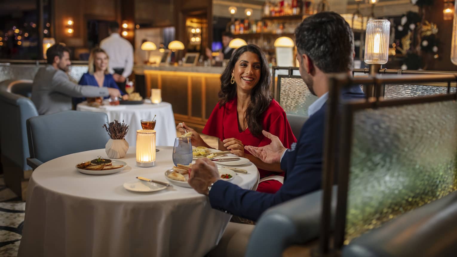Woman in red dress, smiling at man, seated at round dining table in bar lounge