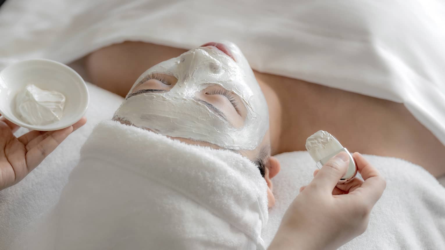 Spa therapist applies white clay mask to woman?s face at the Spa