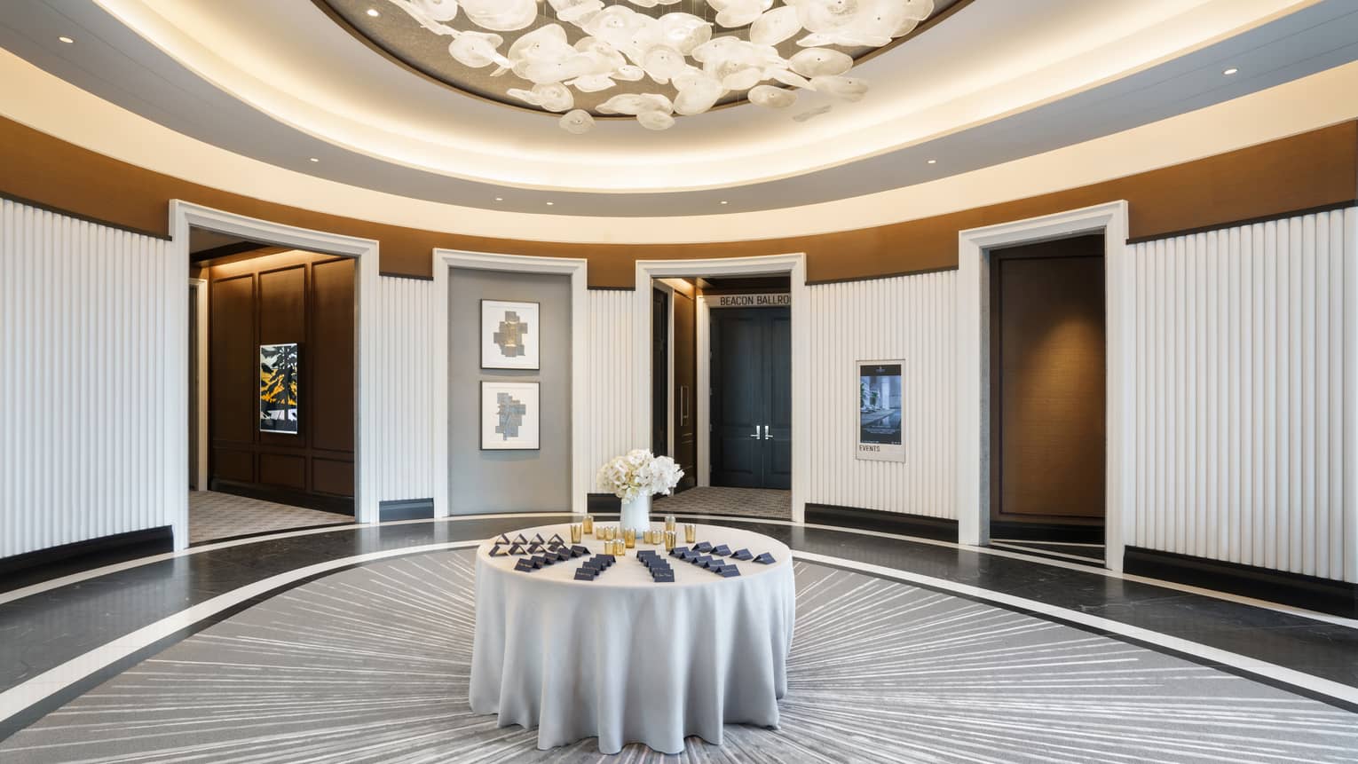 Lobby pre-function are with chandelier, uplighting, round table in middle, grey & gold accents
