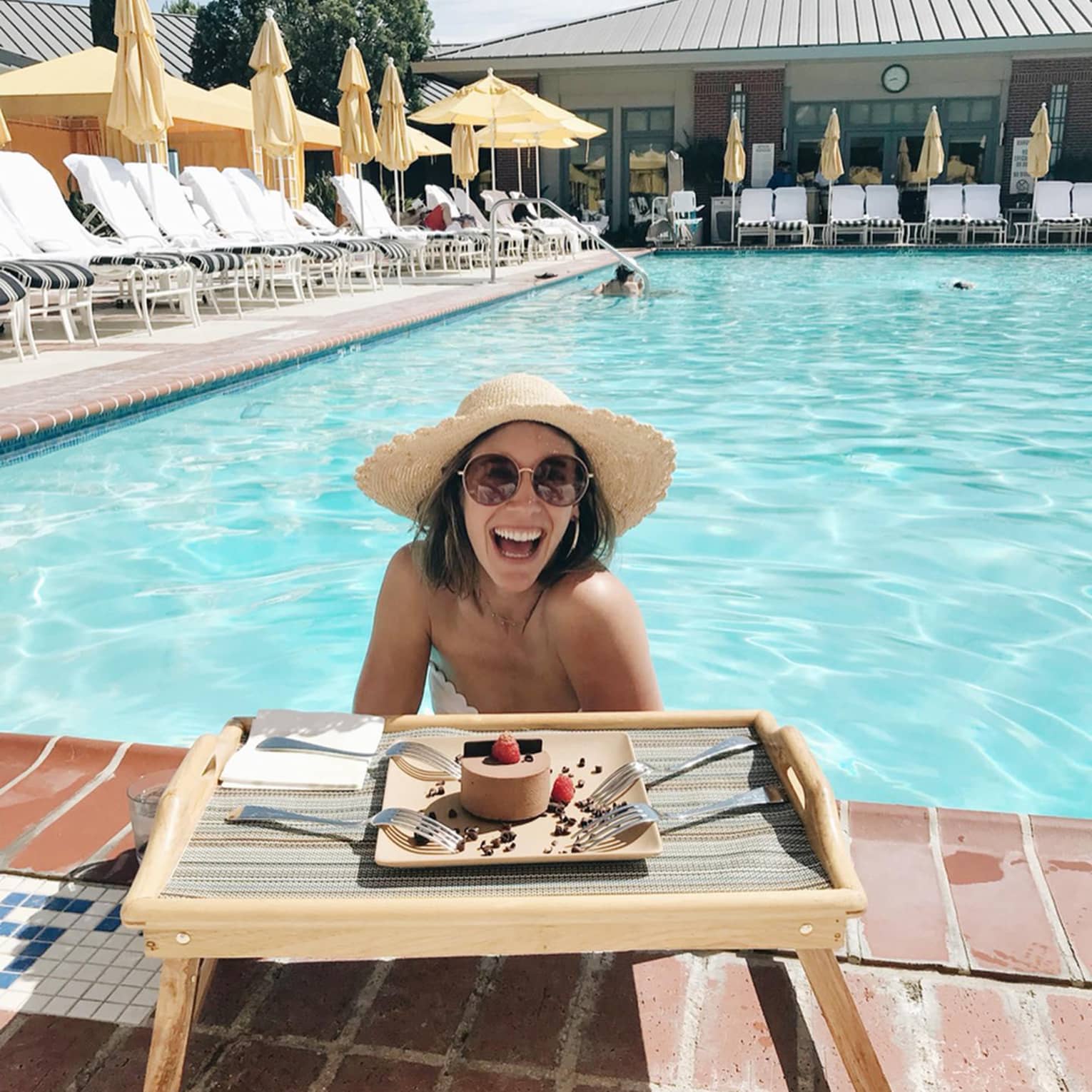 Smiling woman wading in sunny outdoor swimming pool by tray with cake, four forks
