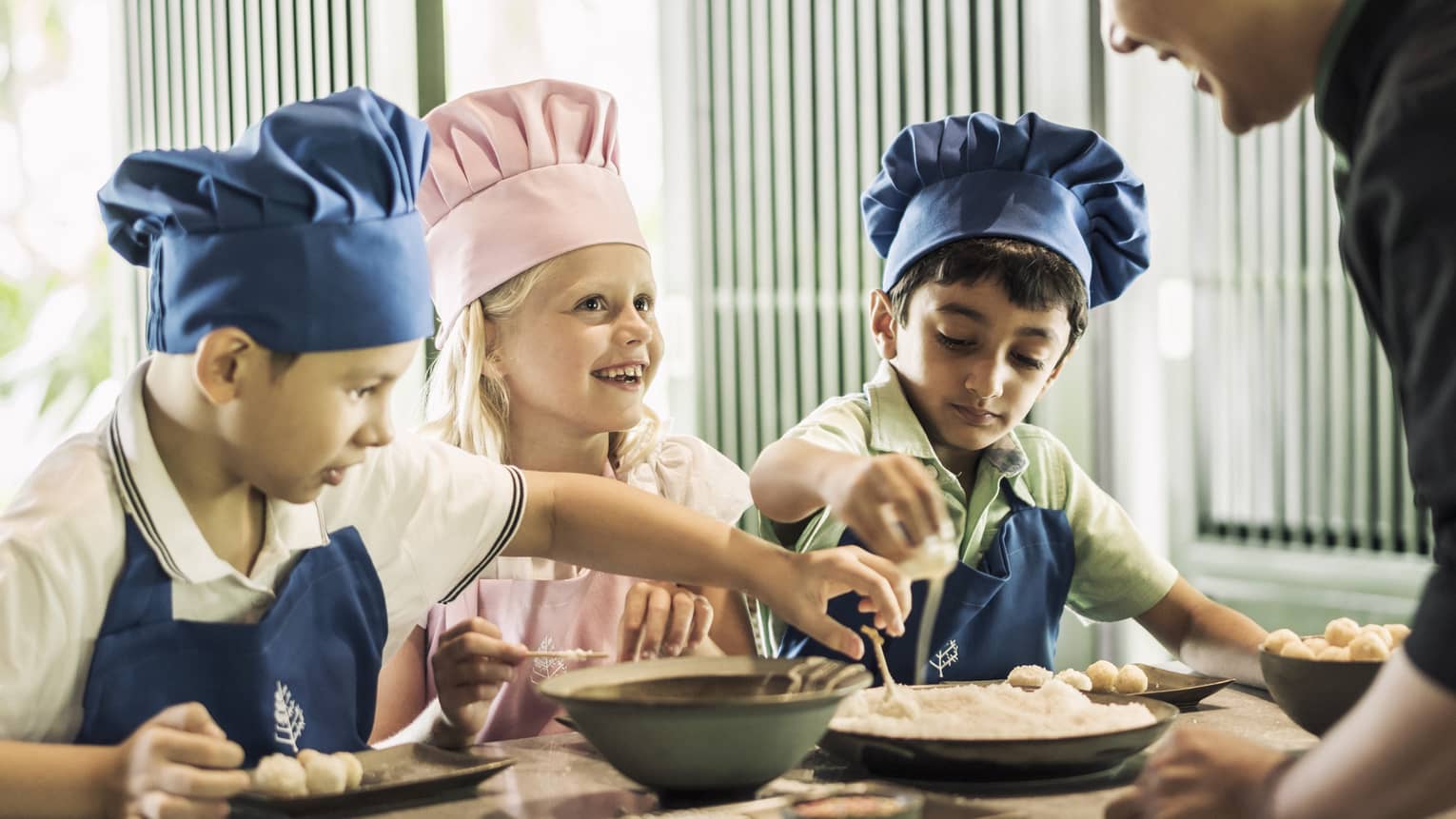 Three children with pink or blue chefs hats making food.