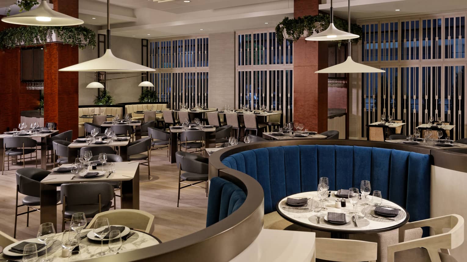 A restaurant with a variety of tables from square to round booths, white lamps hang from the ceiling.