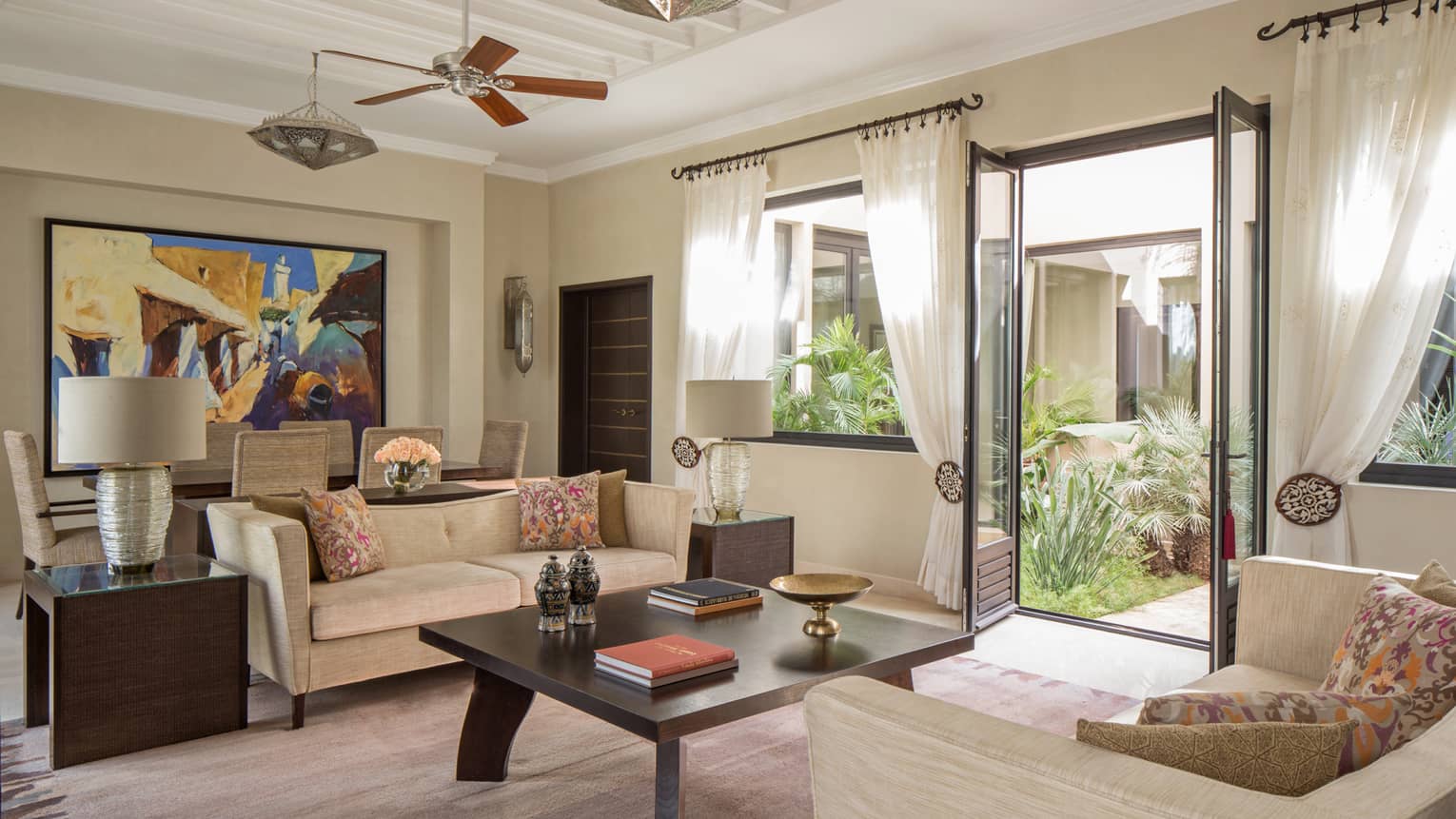 Two Bedroom Villa living room with two sofas around large coffee table with books, dining table, large colourful painting
