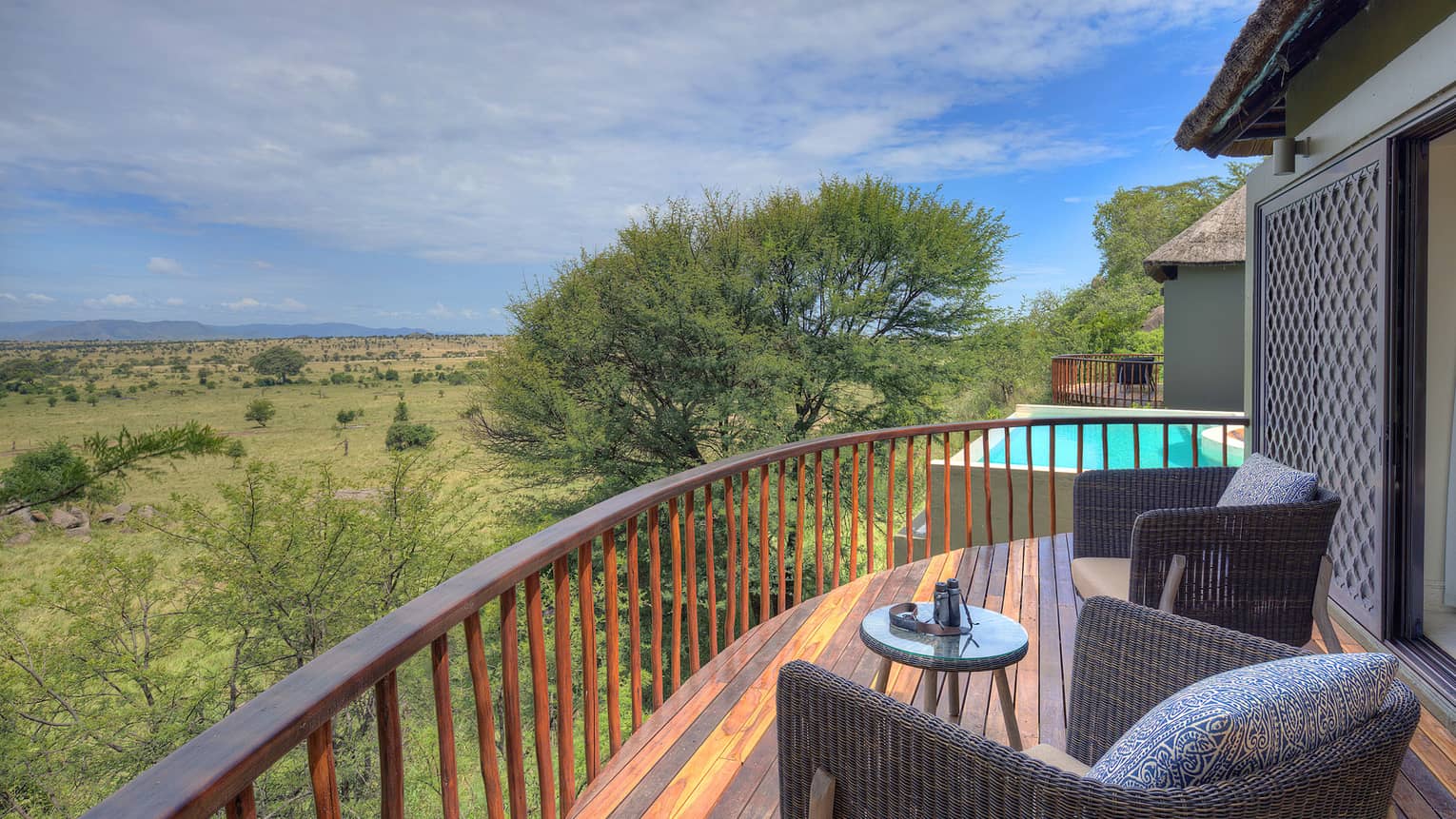Villa balcony with two grey wicker chairs and small table overlooking expansive plains dotted with trees