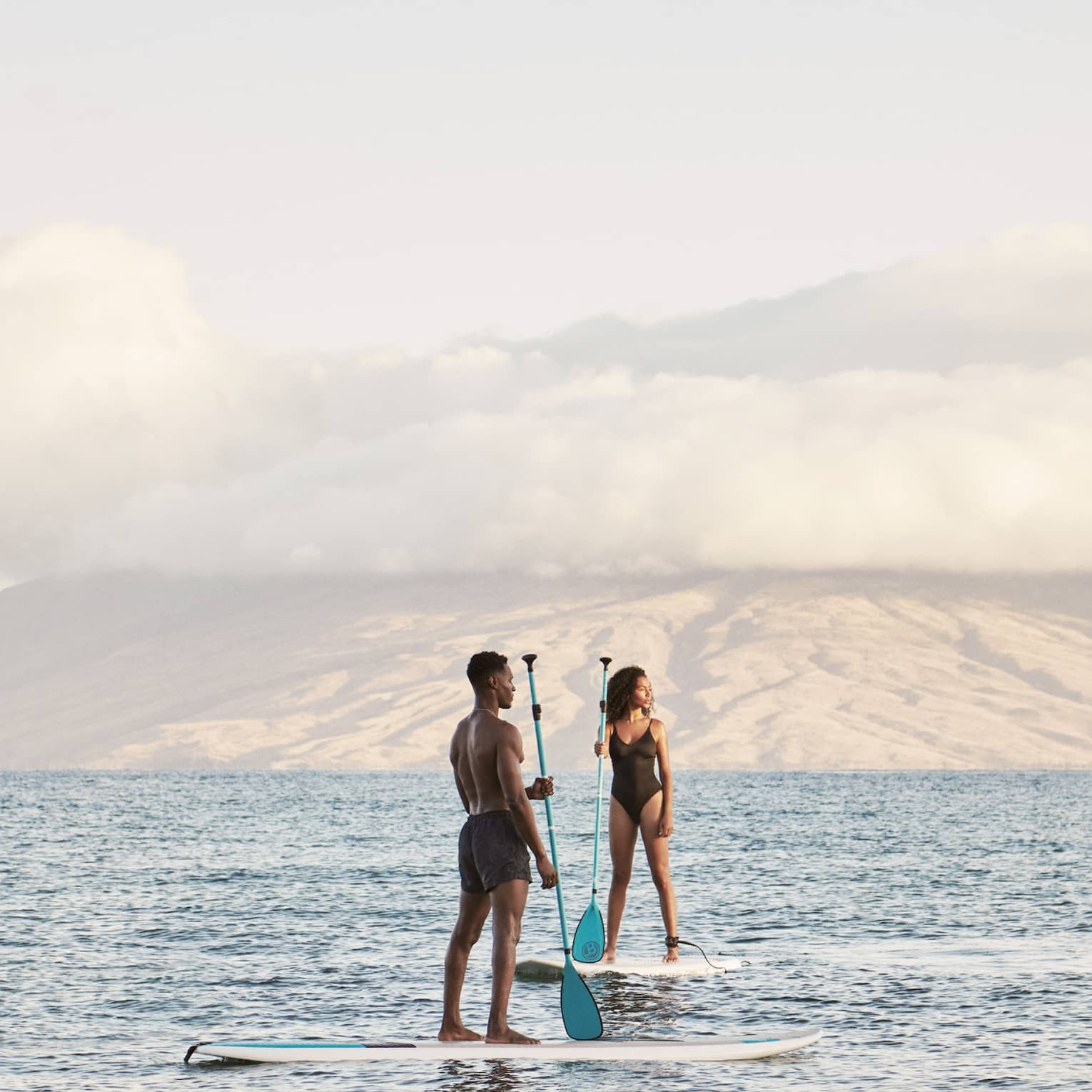 Man and woman stand on SUP paddleboards in the ocean in Maui