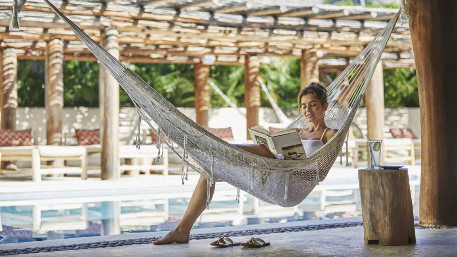 Woman reads book in a hammock next to pool