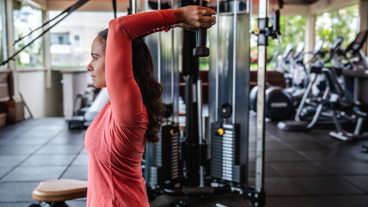 A woman lifts wights above her head at the gym