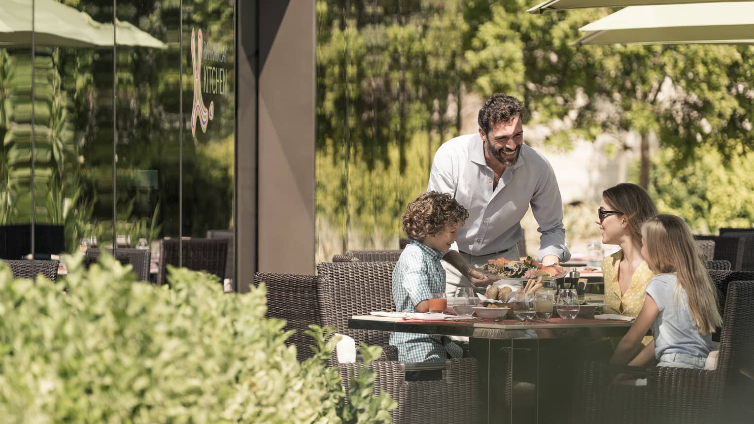 Family of four smiling at outdoor patio table over a meal