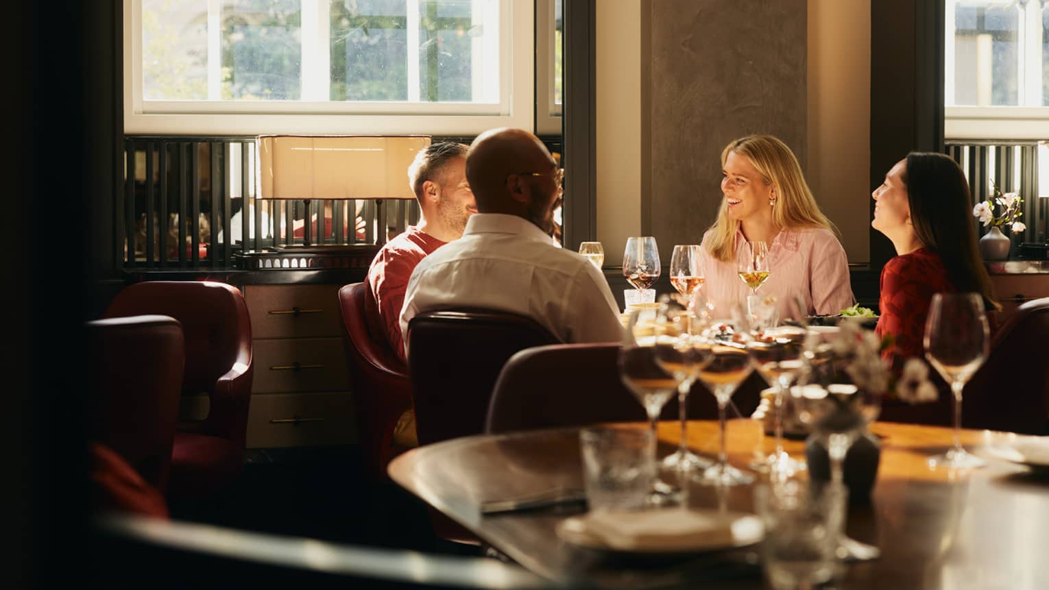 People sitting around a table, enjoying a meal in an indoor dining space. The table is next to a window that is letting in bright natural light.