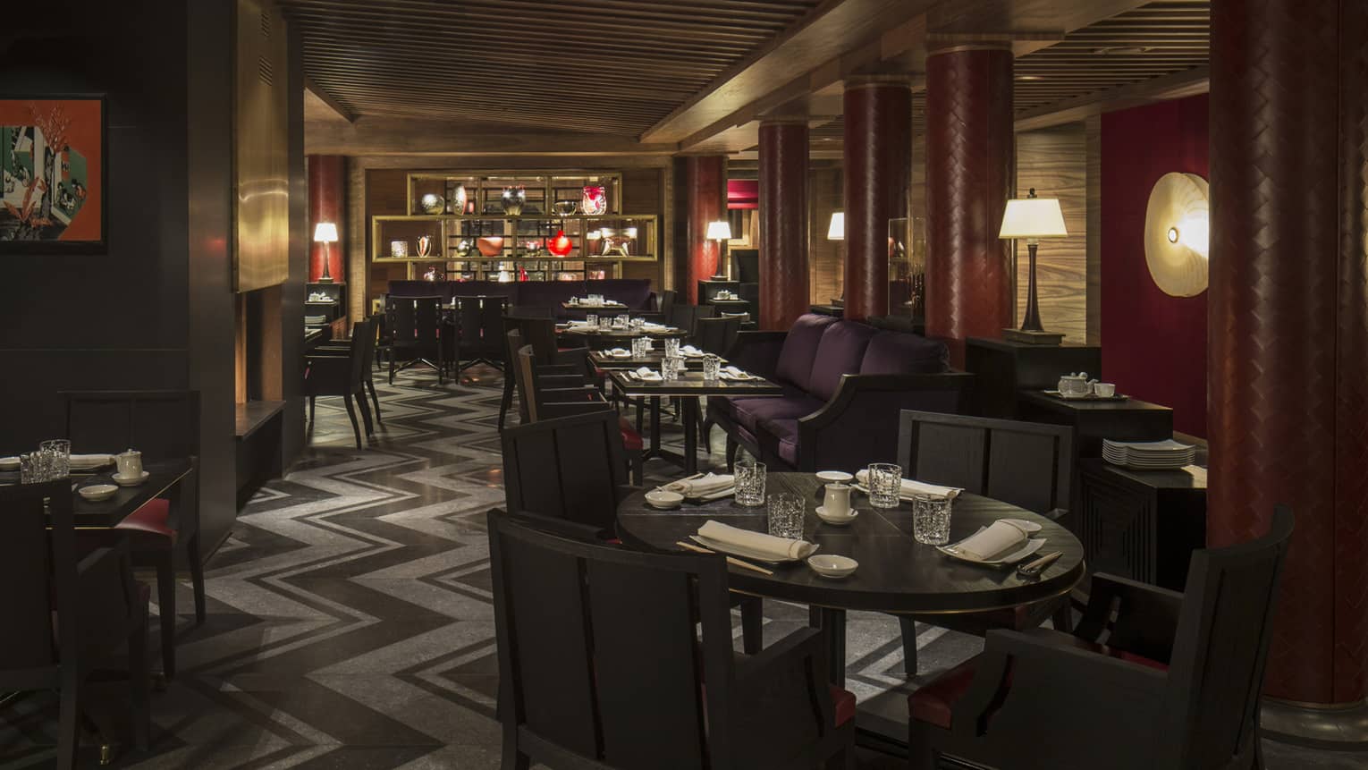 Kaito dimly-lit dining room with round tables, chairs, purple banquettes, red pillars