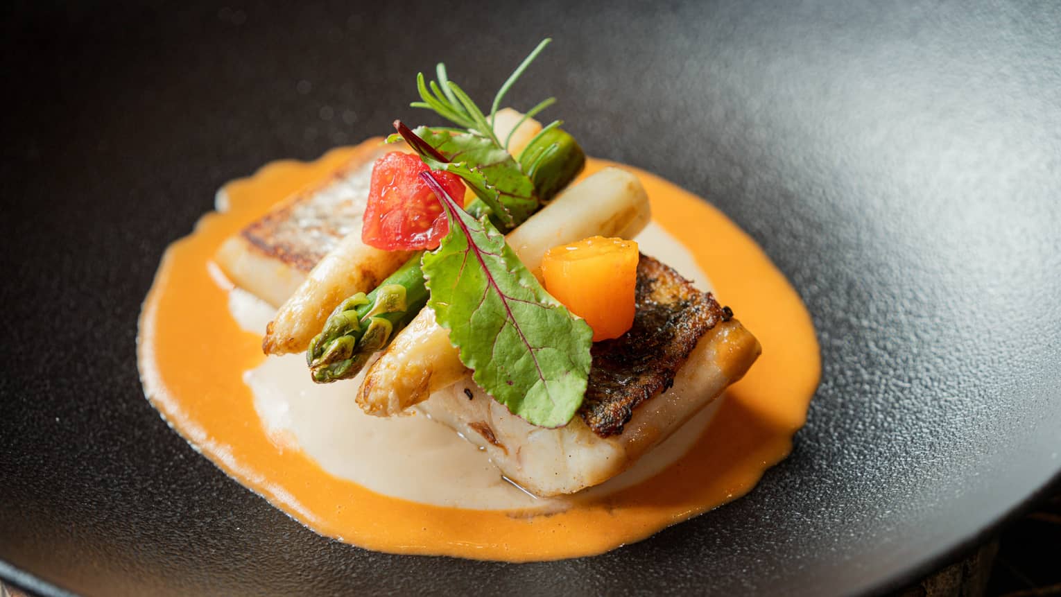 Seared fish topped with asparagus and fresh herbs, served atop an orange sauce