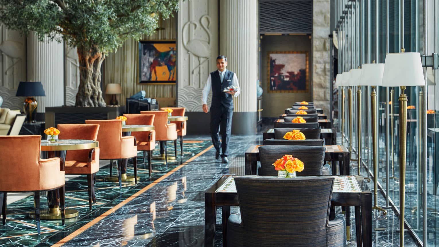 Server in uniform walks across black marble chair, past tables and chairs in sunny Bay-View Lounge