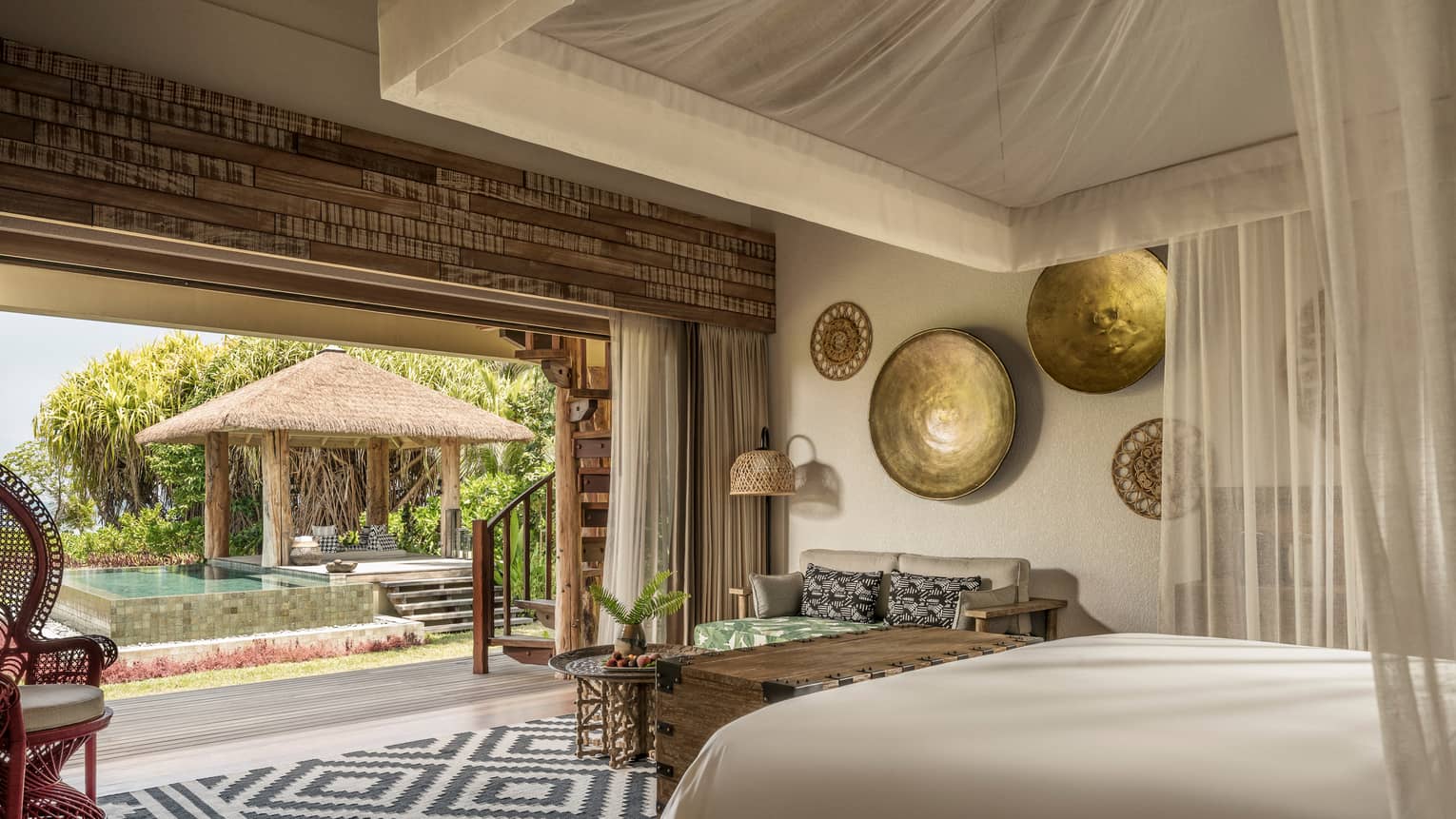 Luxury villa with canopy over bed, artwork on wall, rattan chair opens up to pool