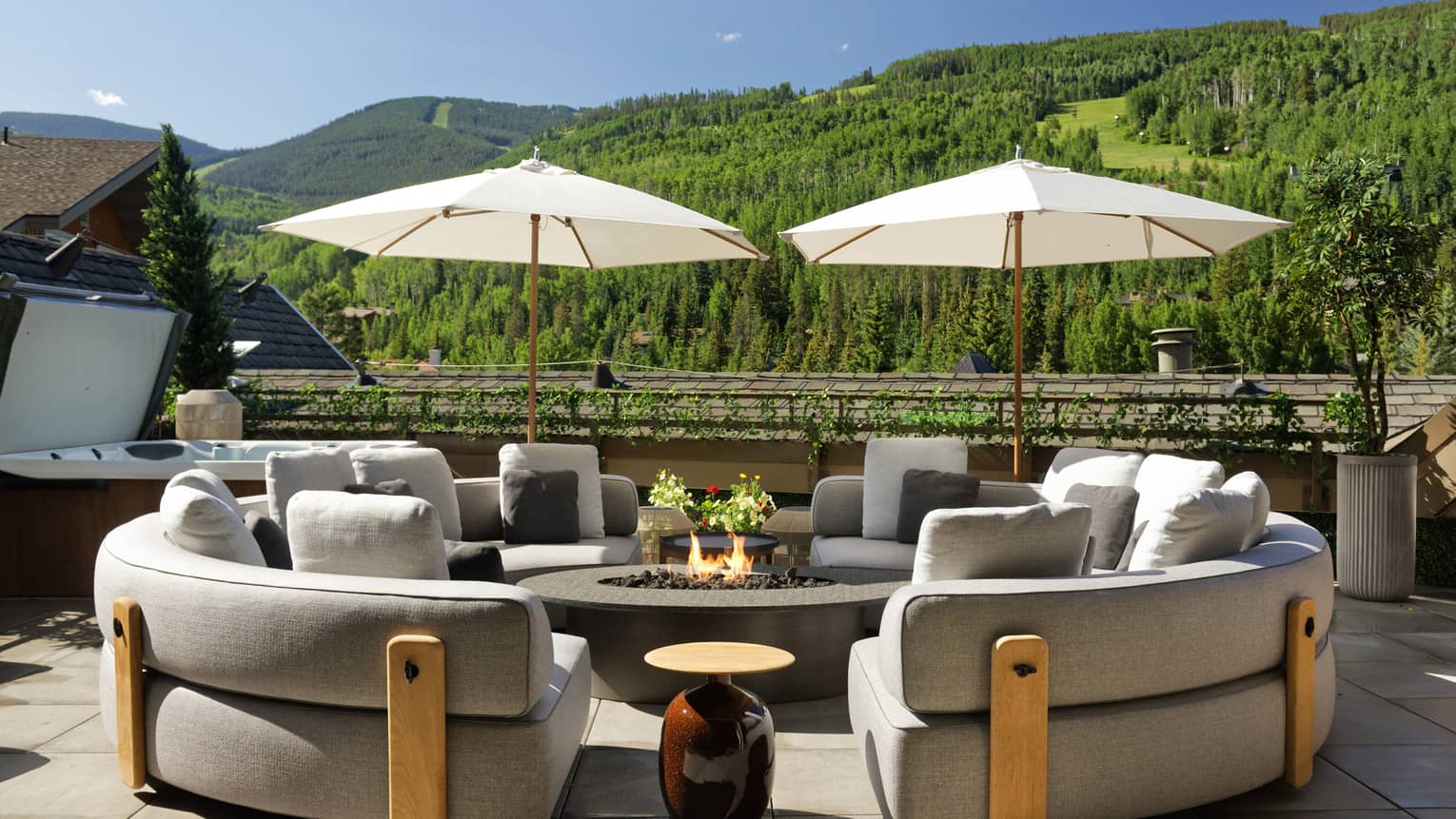 Two curved sofas surround gas fireplace table on terrace with hot tub and mountain view
