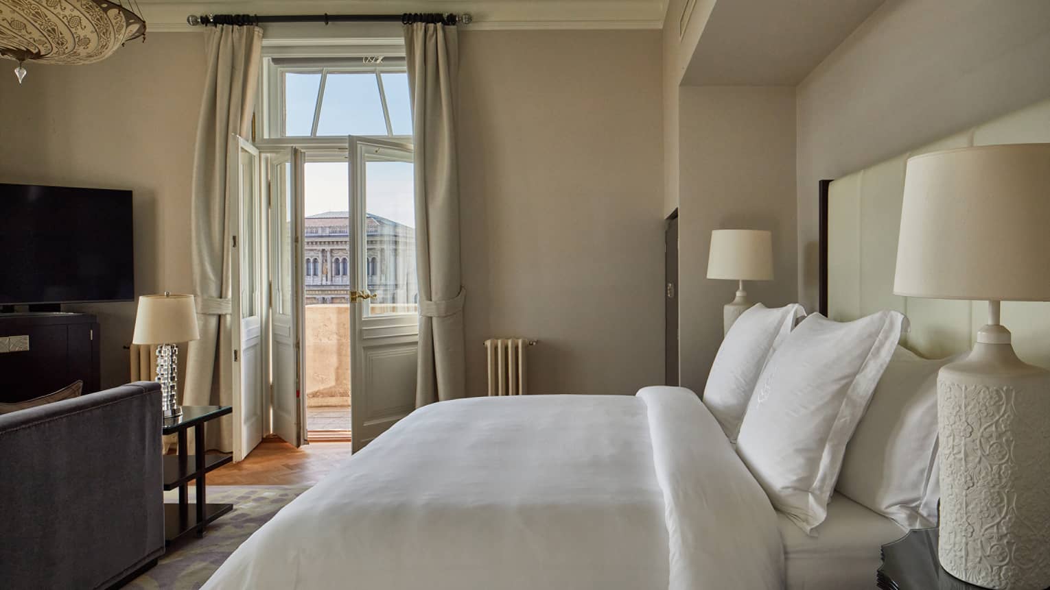 Hotel room with white bedding, large French doors and a terrace view of a historic building