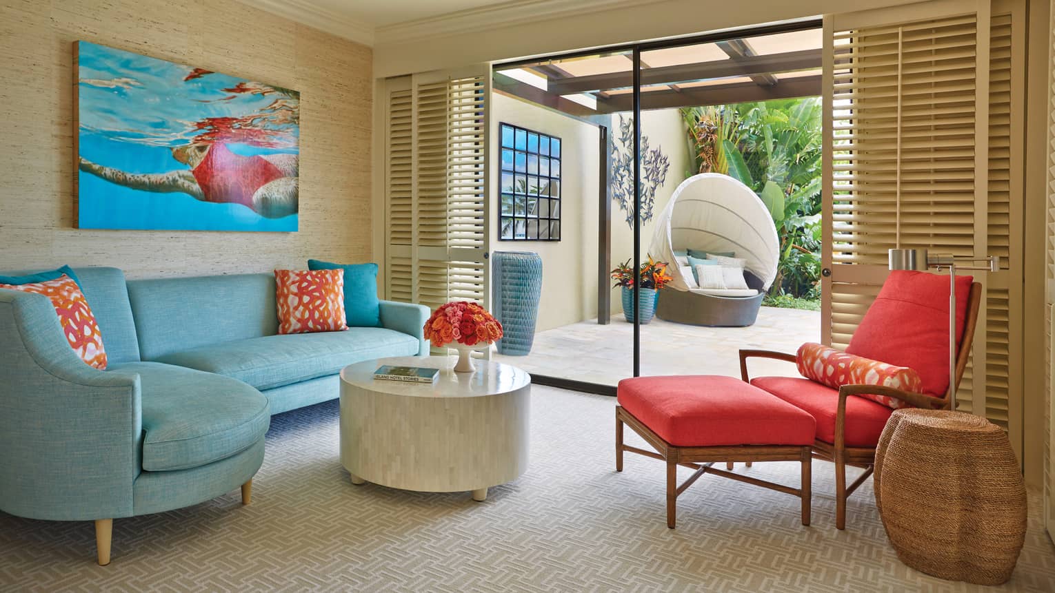 Colourful sitting area with blue sofa, red lounge chair and sliding doors opening to private patio with outdoor seating