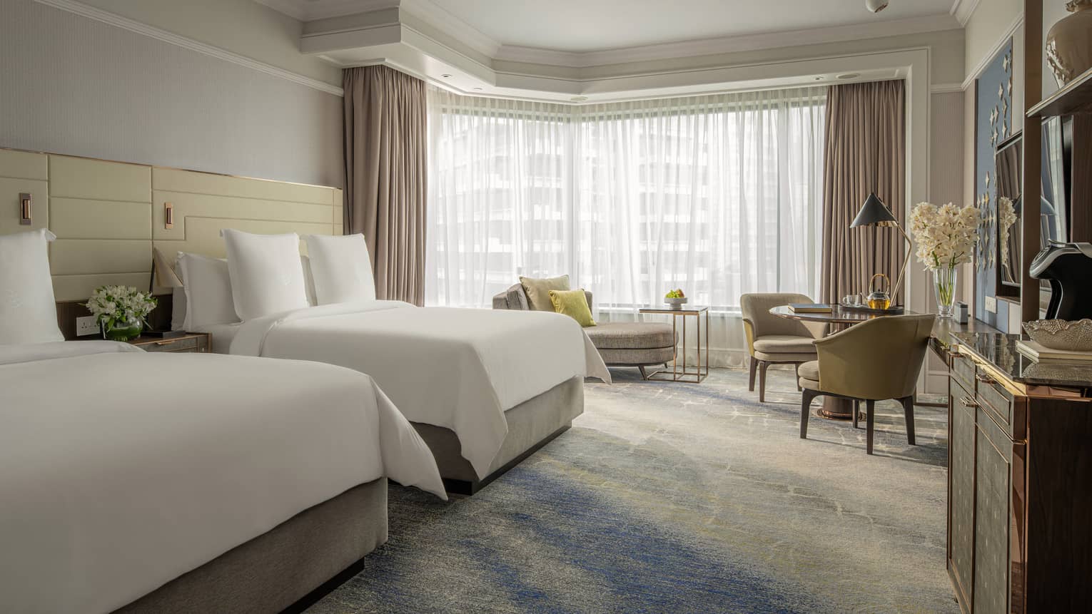 Guest room featuring two queen beds, a seating area and large windows with natural light.