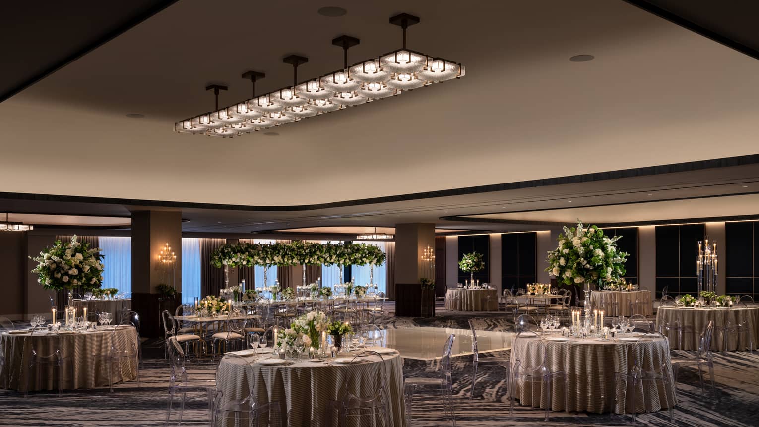 A ballroom with round tables and grey table clothes with flowers and plants as centerpieces on the tables.