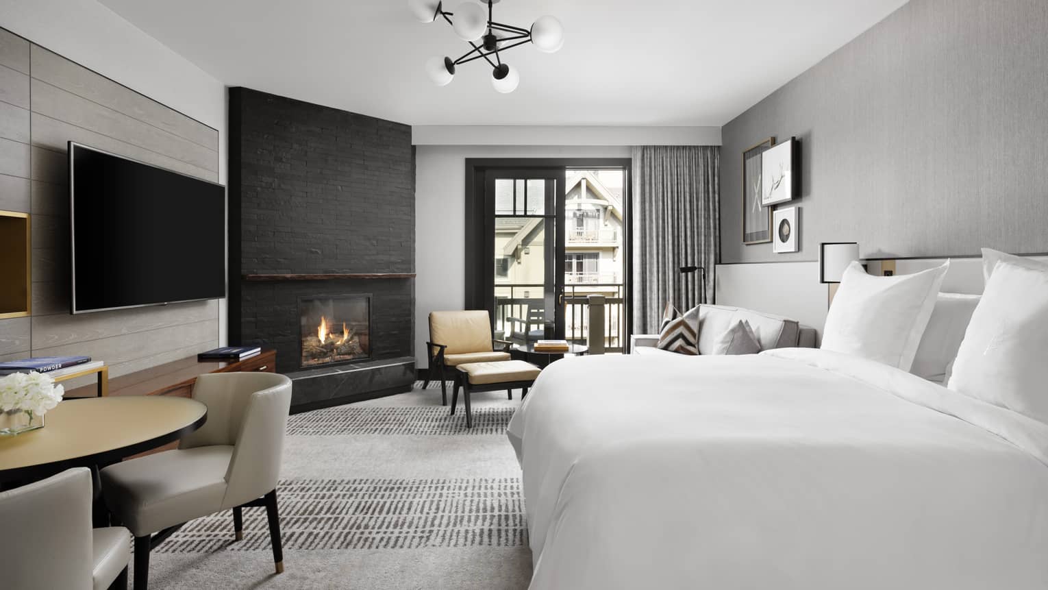 Guest room with King bed, chaise lounge, corner fireplace, round dining table, floor-to-ceiling window with grey curtains, wall-mounted TV