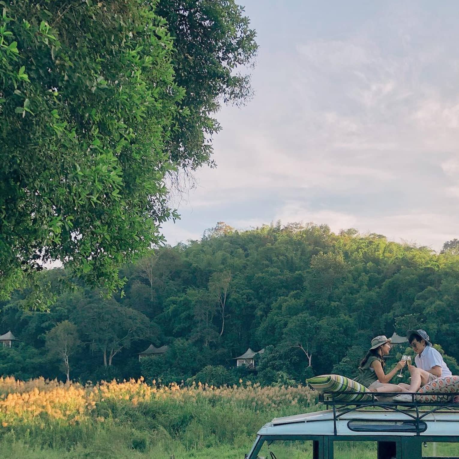 Two guests sit on top of a safari vehicle in a field