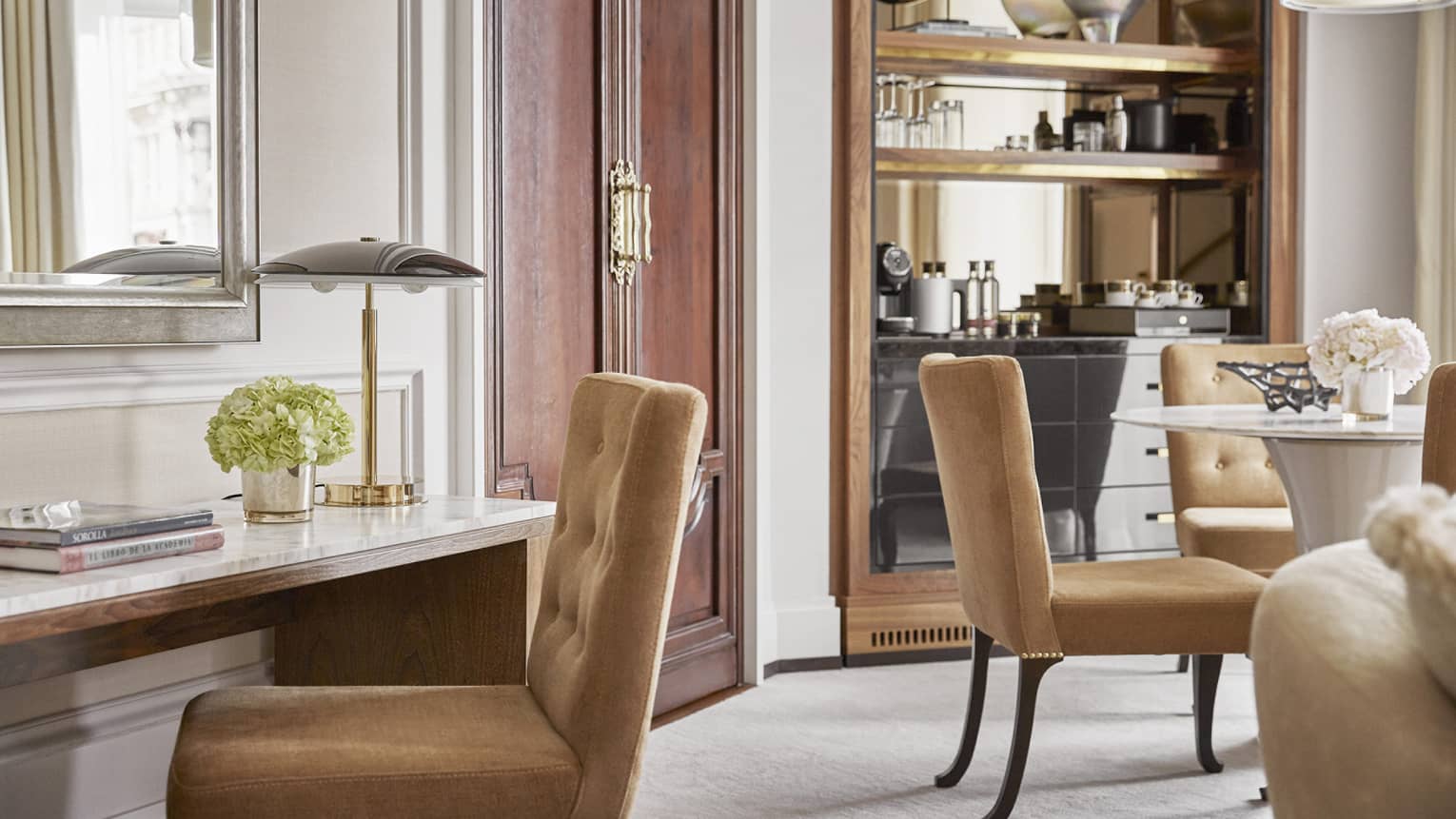 Desk with lamp and light brown chair, and round table with four chairs in the background