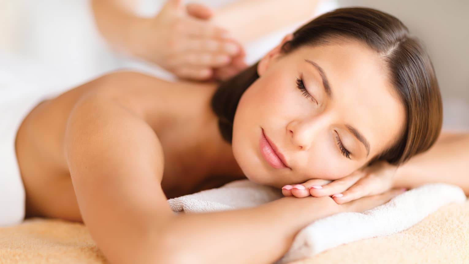 Woman lies on massage table, closes eyes. rests head on arms as spa staff massages back