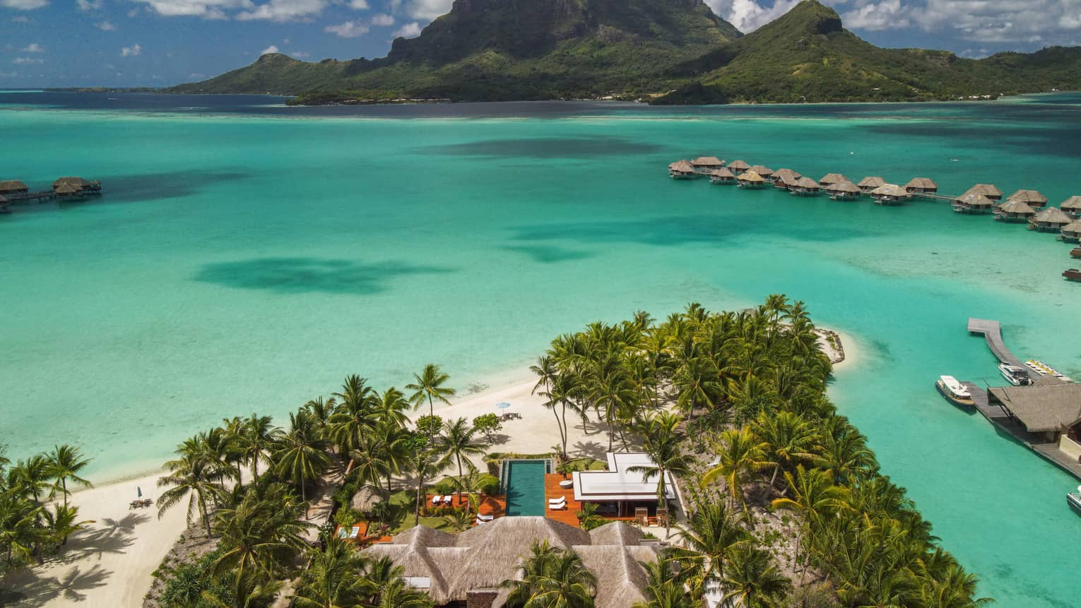 Aerial view of Bora Bora villa on edge of turquoise lagoon, looking out to overwater bungalows and mountains