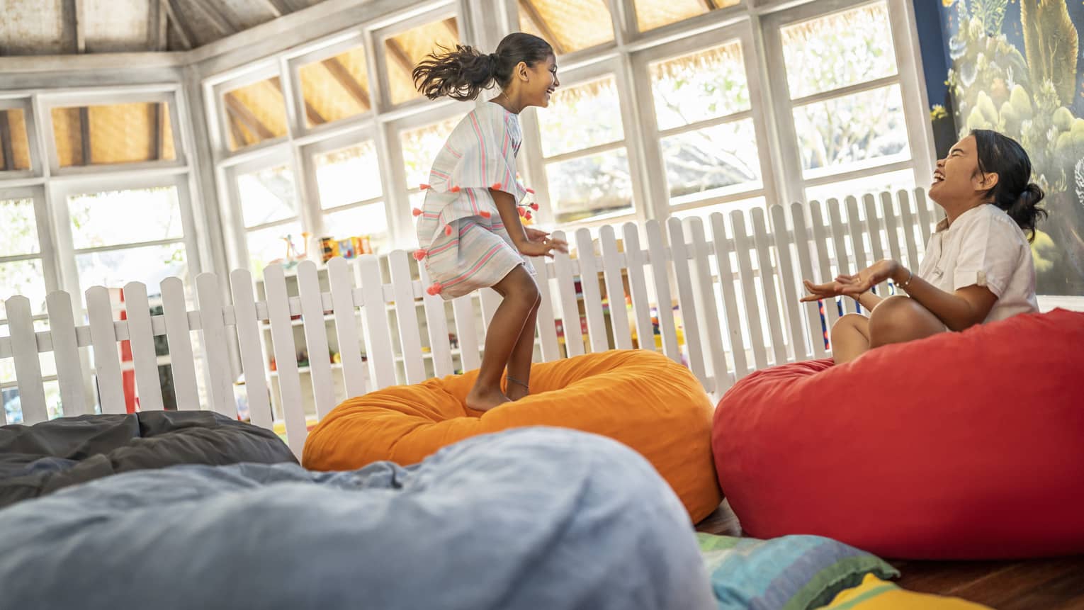 Young girl jumps on bean bag with dedicated attendant in the Kids Club