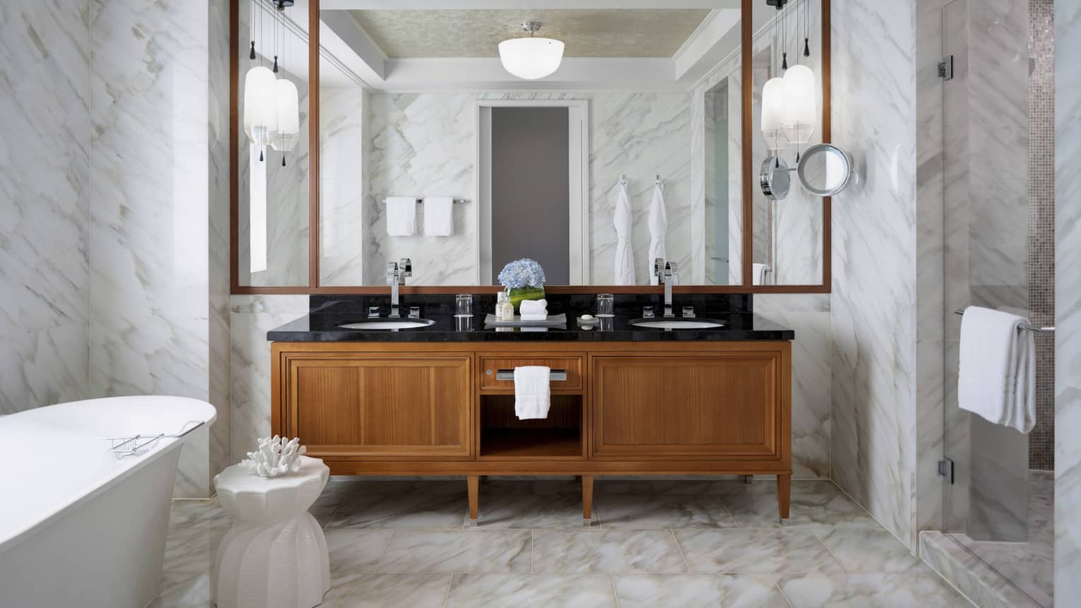 Large bathroom with marble floors and walls, wooden vanity and freestanding tub
