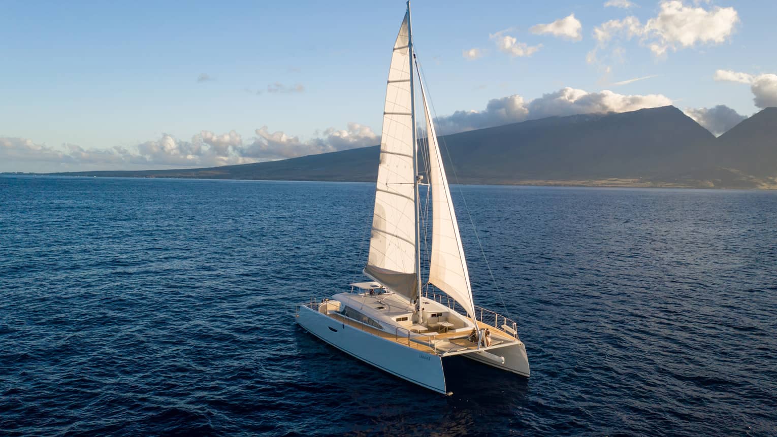 Catamaran sailing on the open water against a mountain backdrop