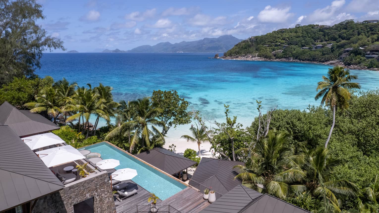 Long rectangular pool of suite in tropical setting with view of beach and lush landscaping